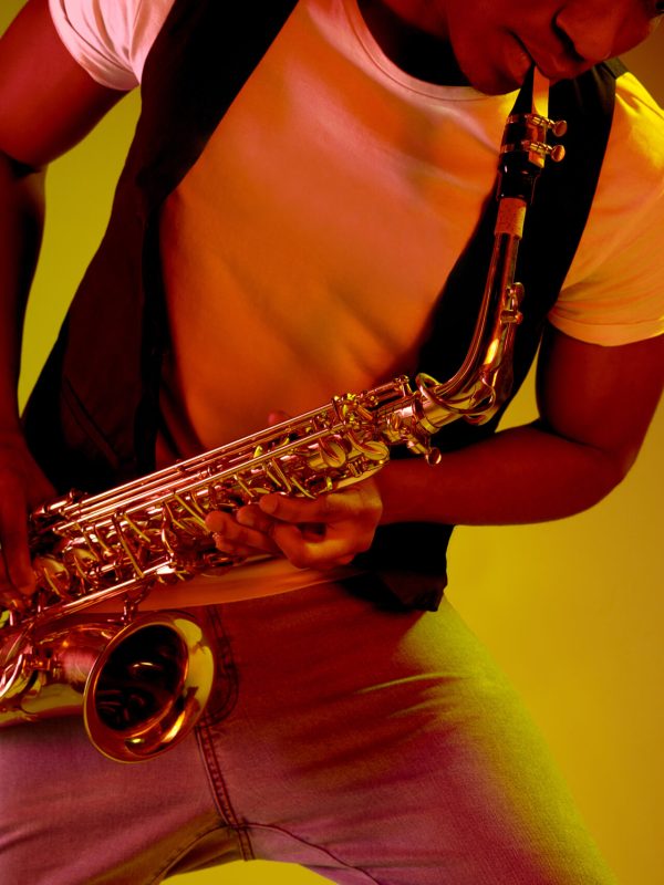 African American handsome jazz musician playing the saxophone in the studio on a neon background. Music concept. Young joyful attractive guy improvising. Close-up retro portrait.